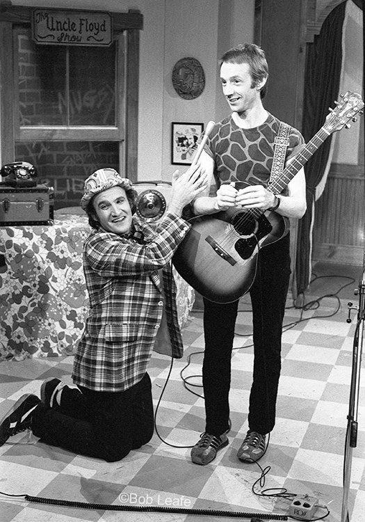 Uncle Floyd kneeling beside Peter Tork holding an acoustic guitar